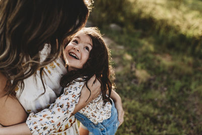 Young happy daughter laughing while being embraced by mother outside