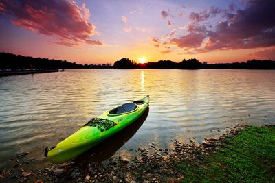 Boat in calm lake against sky during sunset