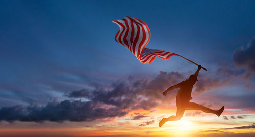 Silhouette woman paragliding against sky at sunset