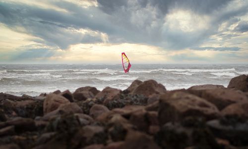 A man windsurfing under dramatic cloudy skies and big waves at silver strand beach, galway, ireland