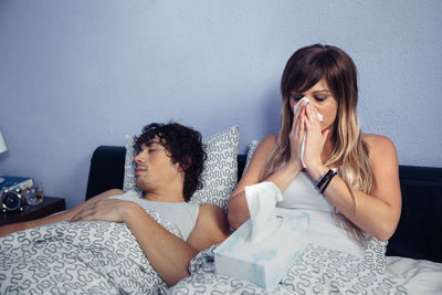 Young woman with man sneezing on bed at home