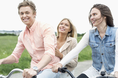 Portrait of happy man enjoying bicycle ride with female friends at countryside