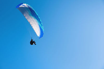 Low angle view of person paragliding against clear blue sky