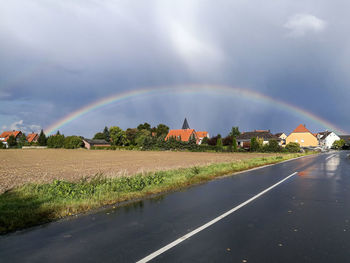Rainbow over road amidst field against sky