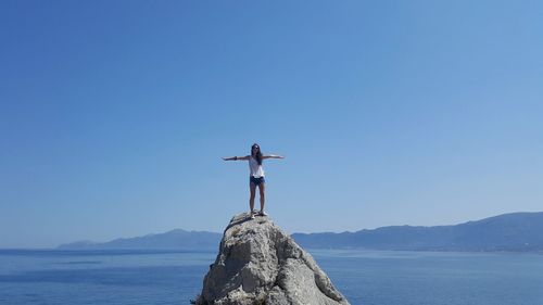 Woman with arms outstretched standing on rock formation against sea at beach