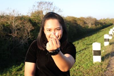 Portrait of smiling young woman gesturing while standing on roadside