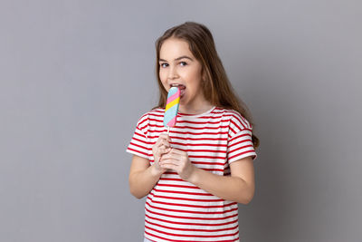 Portrait of young woman holding lollipop against gray background