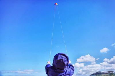 Rear view of boy flying kite against blue sky