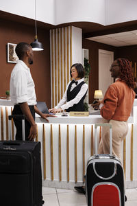 Side view of woman using mobile phone while sitting on suitcase at home