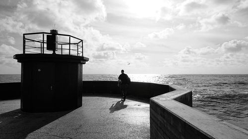 Silhouette man standing on railing by sea against sky