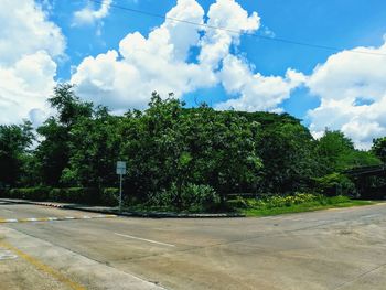 Empty road by trees against sky in city