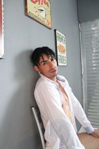 Portrait of transgender young man sitting against wall