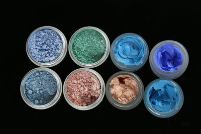 High angle view of colorful make-up product arranged in containers on black background