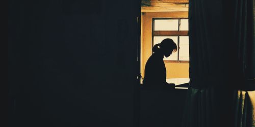 Side view of silhouette woman standing against window