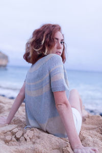 Young woman sitting on beach against clear sky