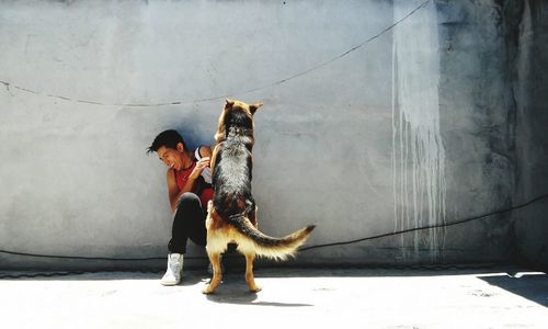 Full length of man playing with dog against wall