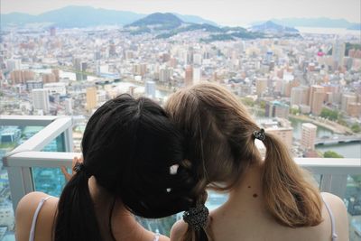 Rear view of sisters with braided hair against window