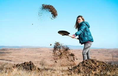 Young woman with shovel on field against clear blue sky