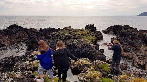 Rear view of women on rocks at beach against sky