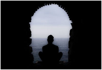 Rear view of silhouette man sitting on rock by sea
