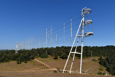 Low angle view of electricity pylon on field against clear blue sky
