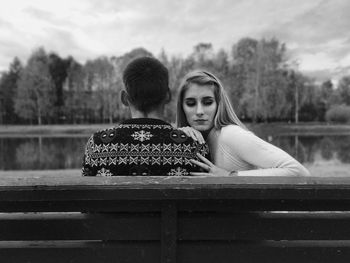 Rear view of couple sitting on bench against lake