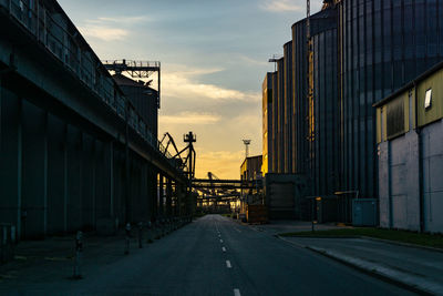 Road amidst buildings against sky during sunset