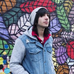 Portrait of young man looking away while standing against graffiti wall