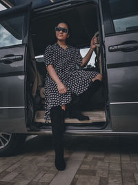 A girl wearing a polkadot dress, sun glasses and high boots sitting in a car 