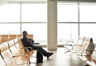 Side view of man sitting on chair in airport