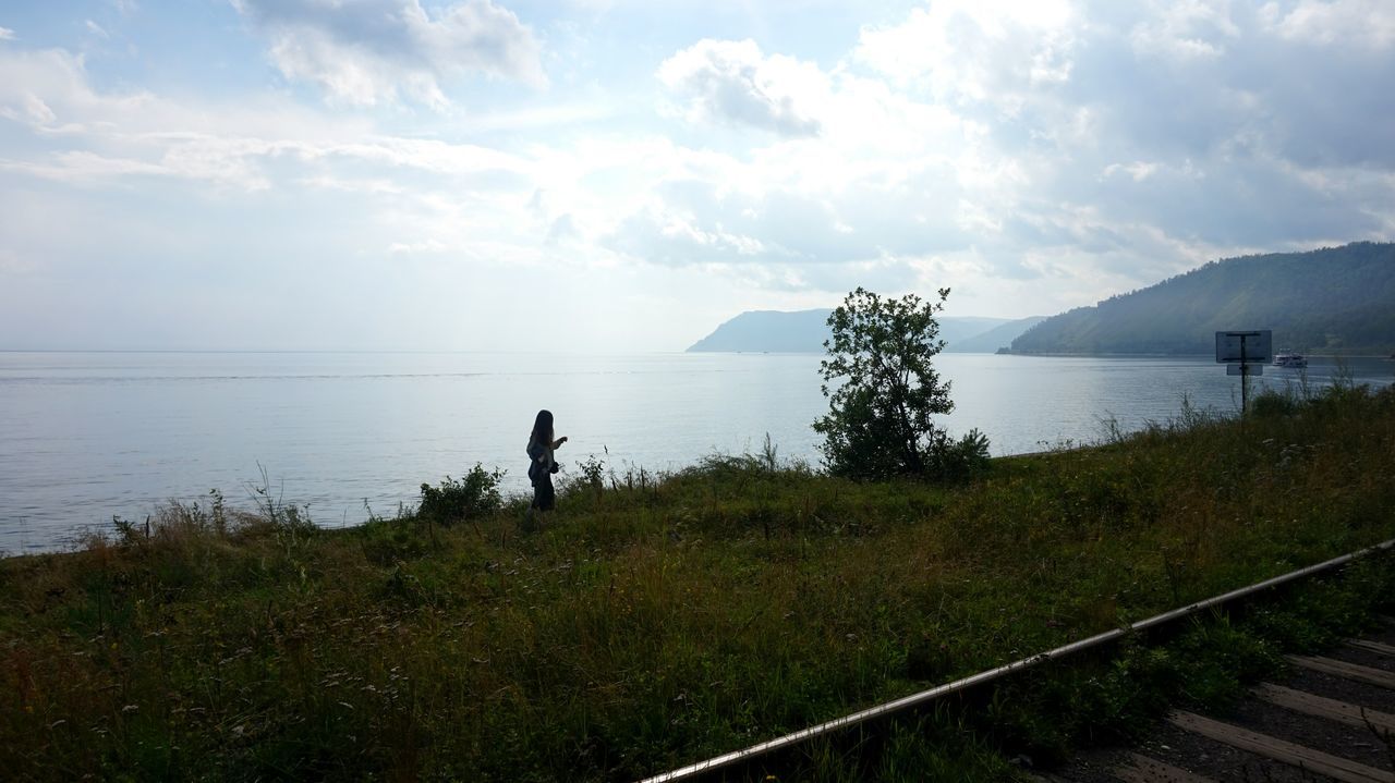 water, grass, sea, tranquil scene, sky, tranquility, lake, scenics, horizon over water, standing, cloud - sky, mountain, beauty in nature, tourism, nature, plant, vacations, lakeshore, remote, cloud, non-urban scene, ocean, seascape, calm, outdoors, standing water, day, coastline, solitude