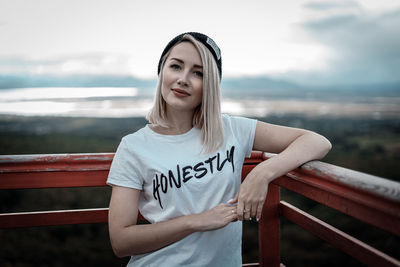 Portrait of smiling woman standing by railing against sky