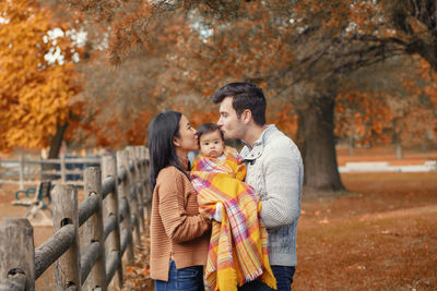 Parents kissing toddler in park during autumn