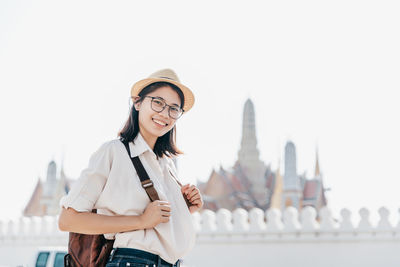 Portrait of smiling young woman standing against clear sky