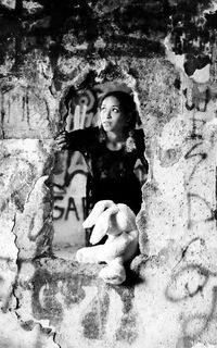 Young woman looking through hole in old abandoned wall