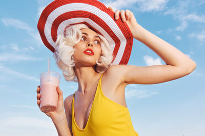 Portrait of smiling young woman with arms raised against sky