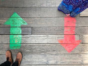 Low section of couple standing on arrow signs on floorboard