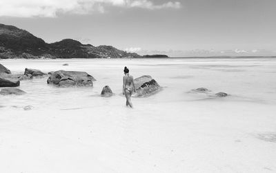 Rear view of woman wearing bikini walking in sea against sky