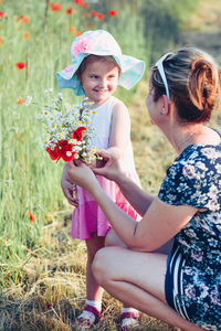 Girl holding flower by mother on grass