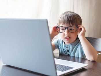 Curious toddler boy explores the laptop and staring on screen through big glasses. 