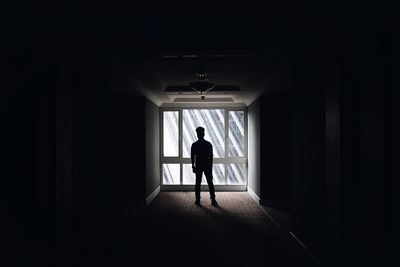 Silhouette man standing in dark corridor against window