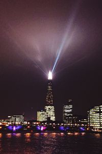 Illuminated city by sea against sky at night