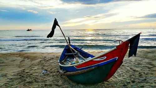 Boat moored on beach against sky during sunset