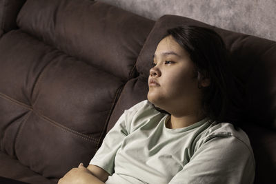 Chubby asian teen girl at home, sitting on the sofa. sad news