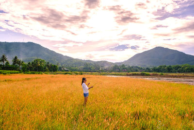 Side view of woman standing at farm against sky during sunset