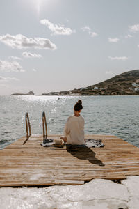 Rear view of woman sitting on pier by sea