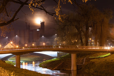 Illuminated bridge over river in city against sky at night