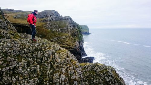 Man standing on cliff by sea against sky