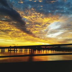 Silhouette bridge over river against sky during sunset