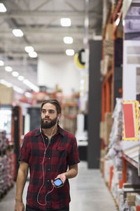 Male customer looking away while listening music through smart phone at hardware store